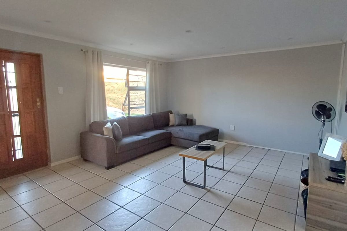Spacious living room featuring neutral wall tones, tiled flooring, and a timber entrance door, providing a bright and functional open-plan living space.