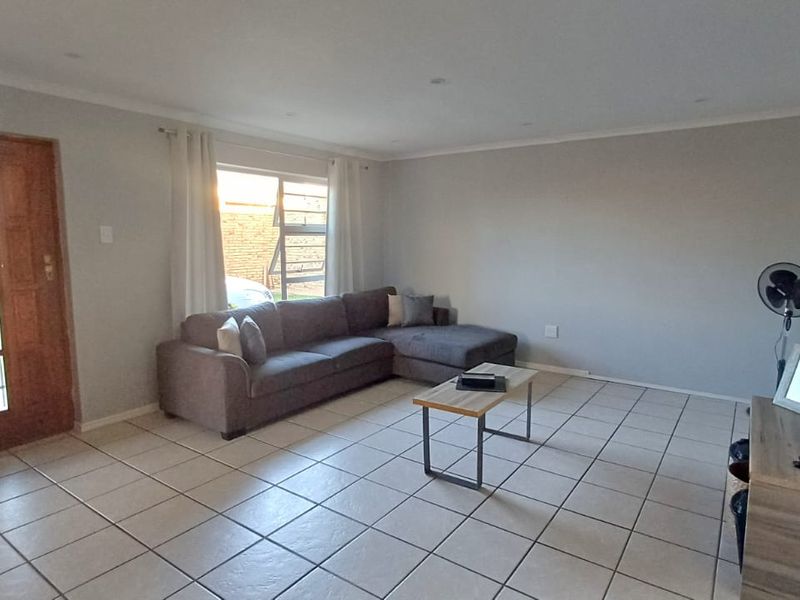 Spacious living room featuring neutral wall tones, tiled flooring, and a timber entrance door, providing a bright and functional open-plan living space.