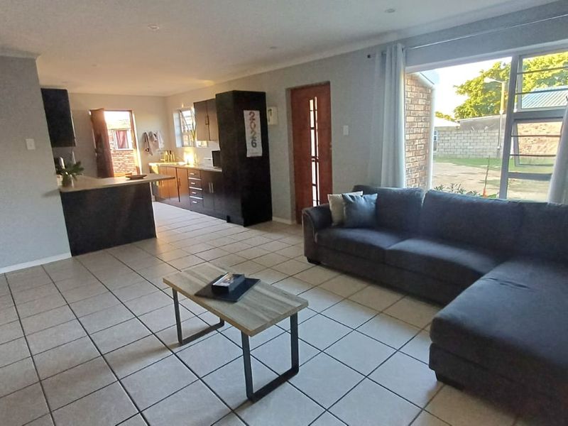 Open-plan living area featuring tiled flooring, recessed lighting, and a functional kitchen with built-in cabinetry and an island, flowing towards the exterior entrance.