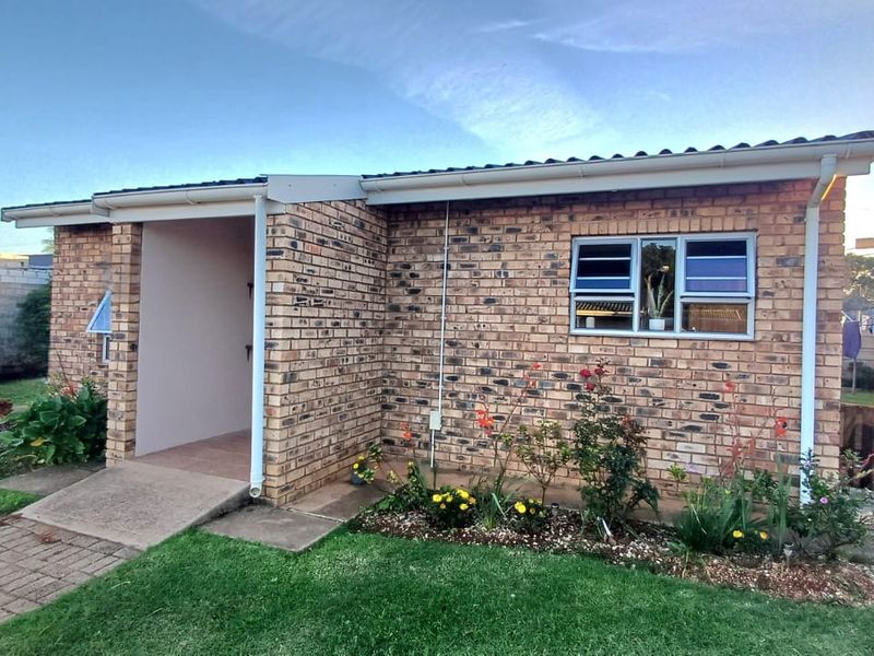 A well-maintained townhouse exterior featuring a classic face brick facade, tiled roof, and a paved entrance walkway with established garden beds.