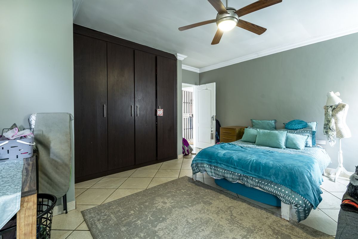 A bedroom featuring dark wood built-in cupboards, tiled flooring, and a ceiling fan, offering a functional space with neutral wall tones.