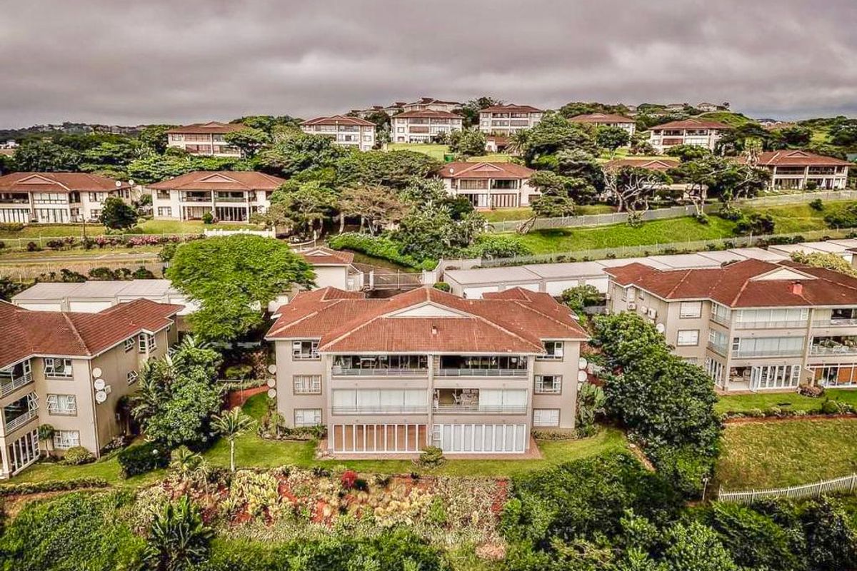 An aerial view of a residential apartment complex featuring tiled roofs, private balconies, and well-maintained landscaped gardens in a suburban setting.