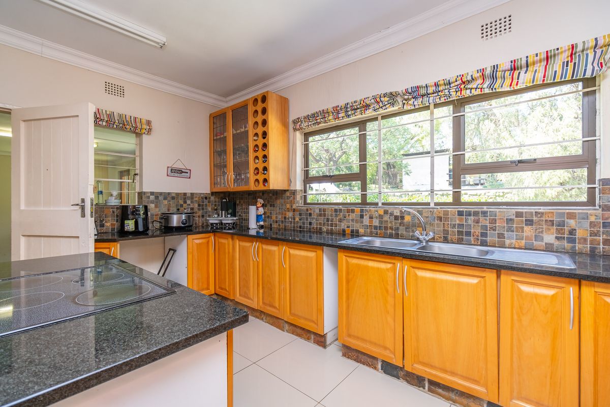 A functional kitchen featuring wooden cabinetry, granite countertops, a double basin sink, and a built-in electric hob with a tiled backsplash.