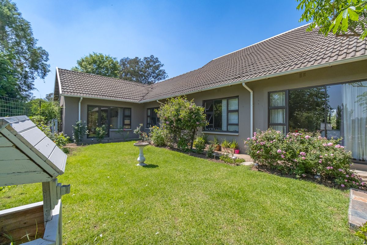 Rear view of the property featuring a well-maintained lawn, established garden beds, and a tiled roof structure with aluminium window frames.