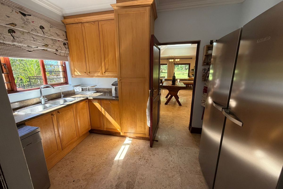 A functional kitchen featuring warm wooden cabinetry, granite countertops, and stone tile flooring, with a view through to the adjacent dining area.