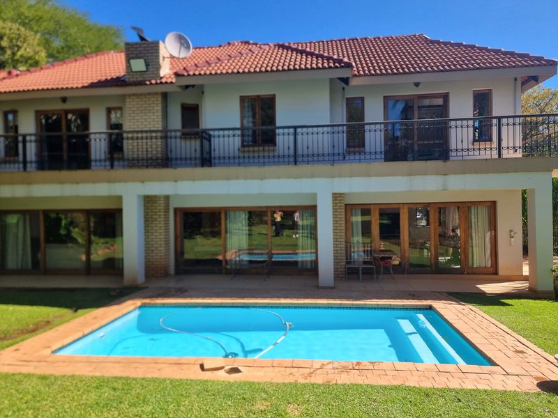 Rear view of a two-story house featuring a swimming pool, a ground-floor patio, and an upper-level balcony with wrought iron railings.