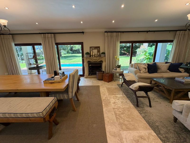 Spacious open-plan living and dining area featuring elegant travertine flooring, a classic stone fireplace, and large sliding doors opening to the pool and garden.