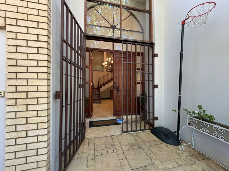Main entrance featuring a secure metal gate, timber front door, and an arched transom window leading into a tiled foyer with a staircase.