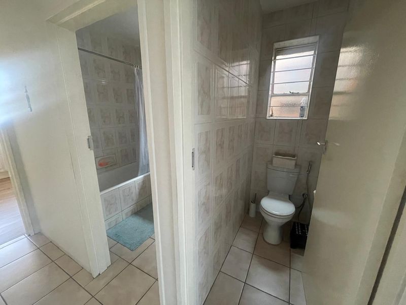 A functional bathroom featuring a separate toilet area and a bathtub with shower combination, finished with classic ceramic wall and floor tiles.