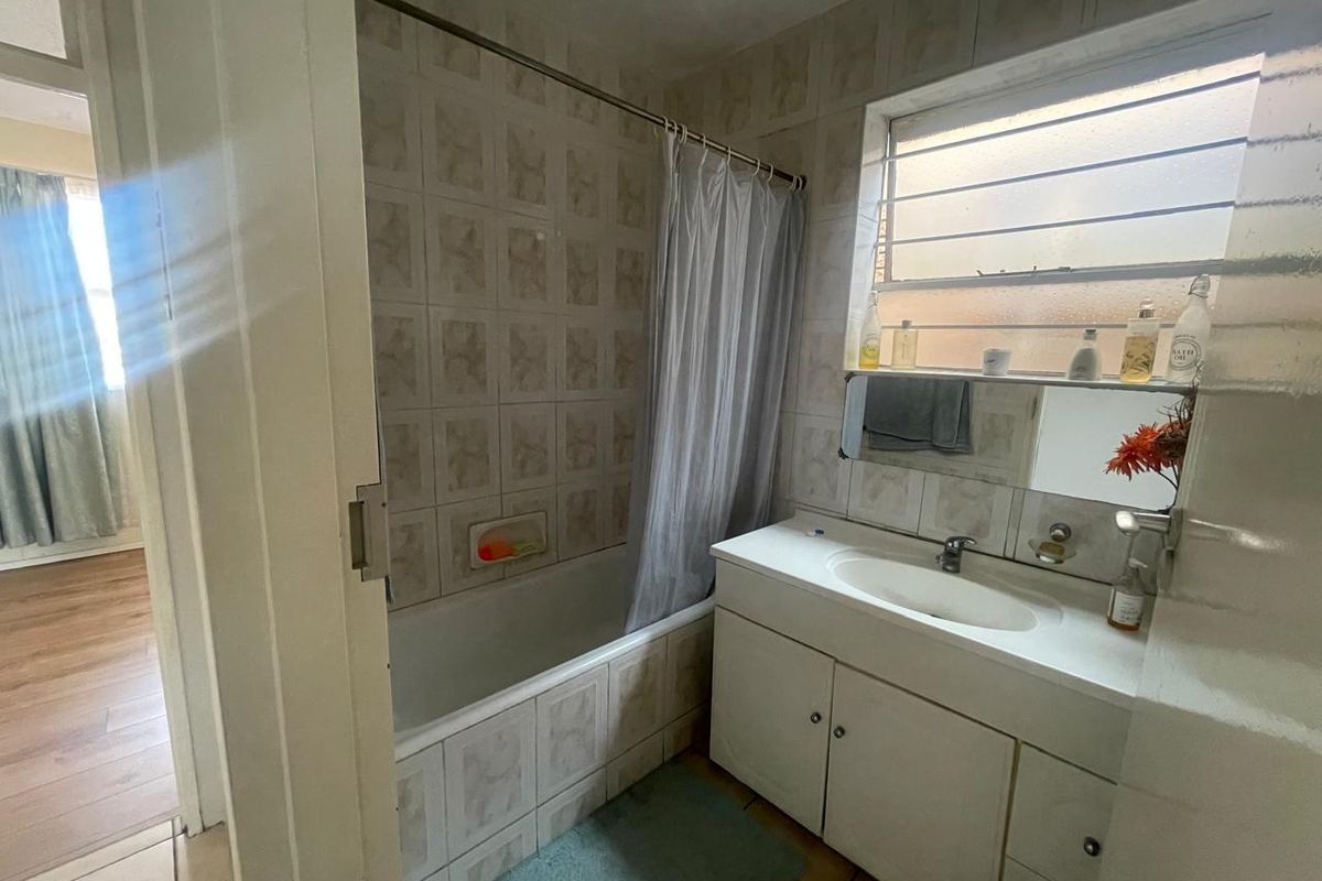 A dated bathroom featuring a built-in bathtub with shower curtain, a vanity unit with integrated basin, and tiled wall finishes.