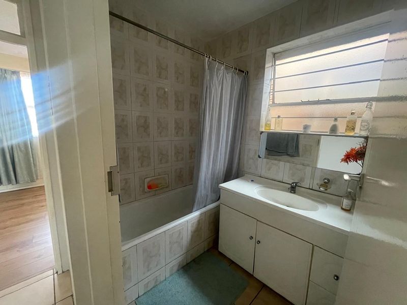 A dated bathroom featuring a built-in bathtub with shower curtain, a vanity unit with integrated basin, and tiled wall finishes.