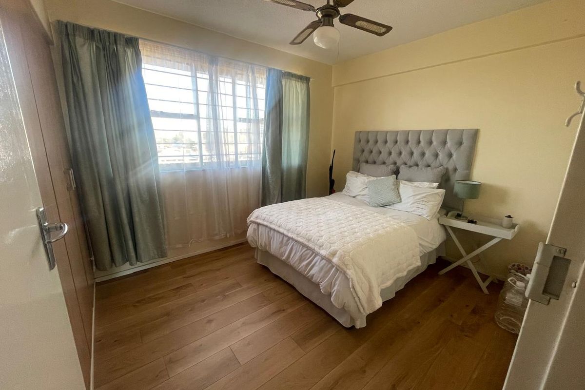 A bedroom featuring wood-look flooring, a ceiling fan, and a window with security bars.