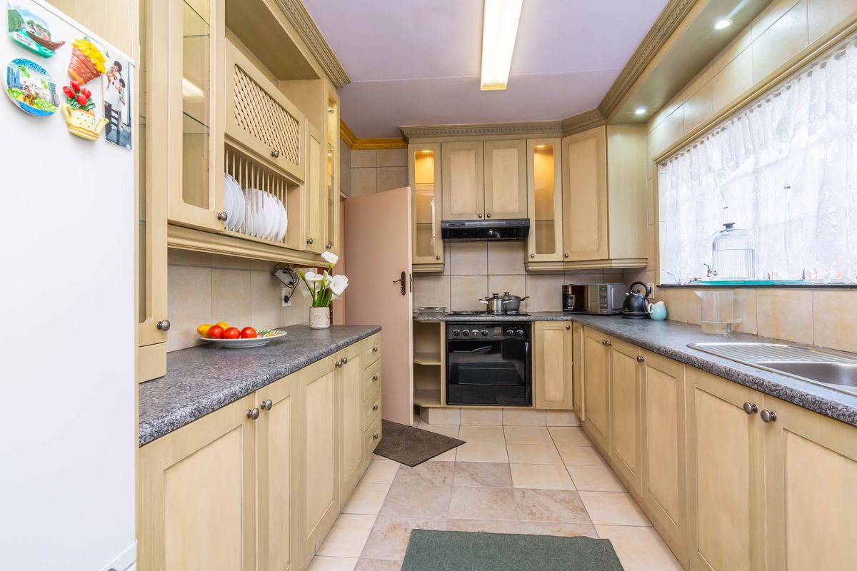 A functional kitchen featuring light-toned built-in cabinetry, granite countertops, a built-in oven with extractor fan, and tiled flooring throughout.