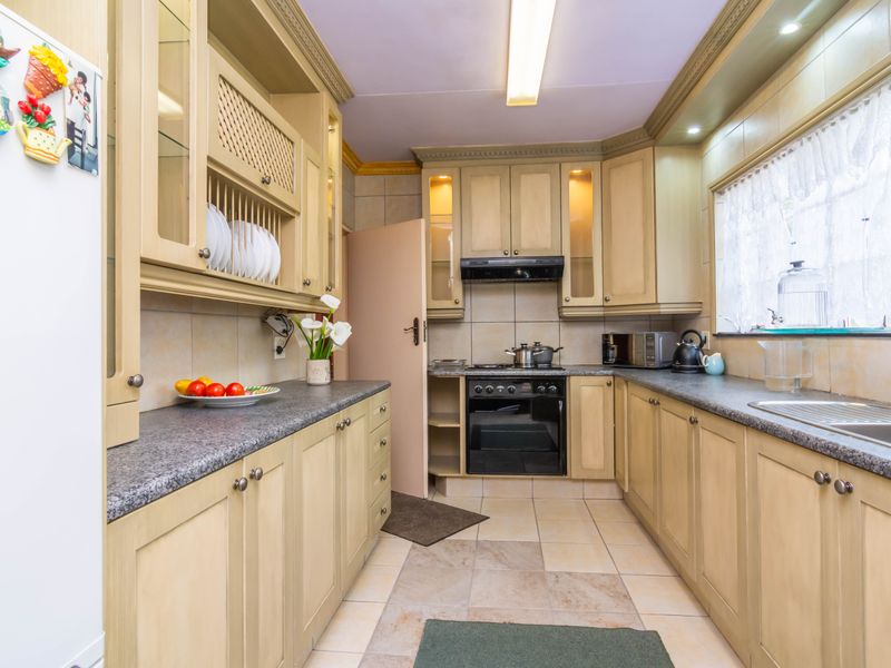 A functional kitchen featuring light-toned built-in cabinetry, granite countertops, a built-in oven with extractor fan, and tiled flooring throughout.