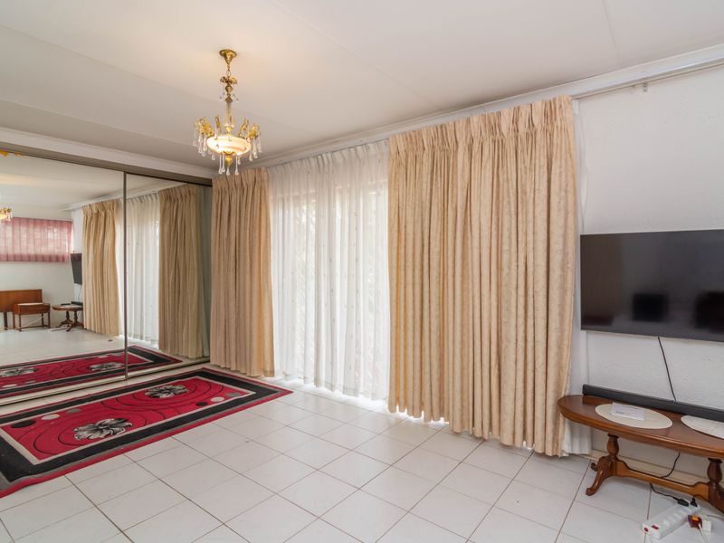 A living room featuring tiled flooring, a ceiling chandelier, and large mirrored sliding wardrobe doors, providing a bright and spacious feel.