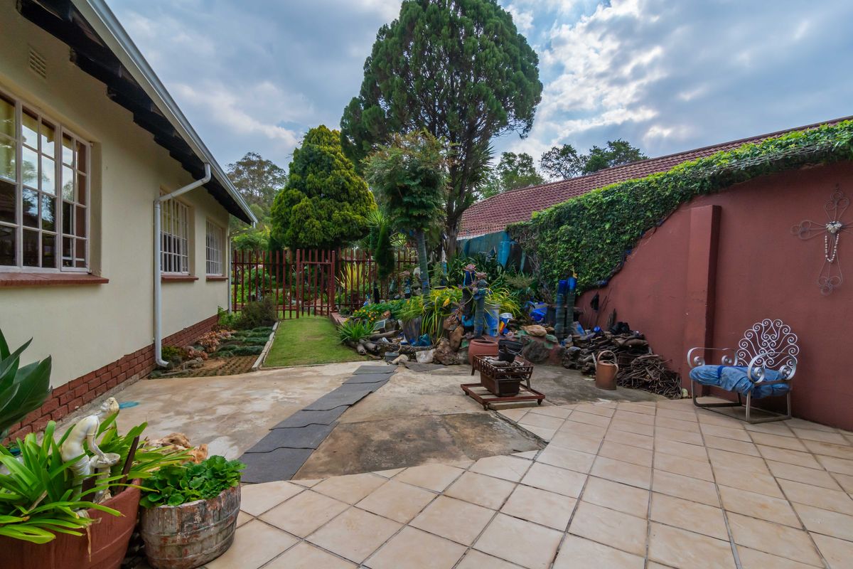Rear exterior area featuring a tiled patio, concrete paving, and a boundary wall with established garden elements.