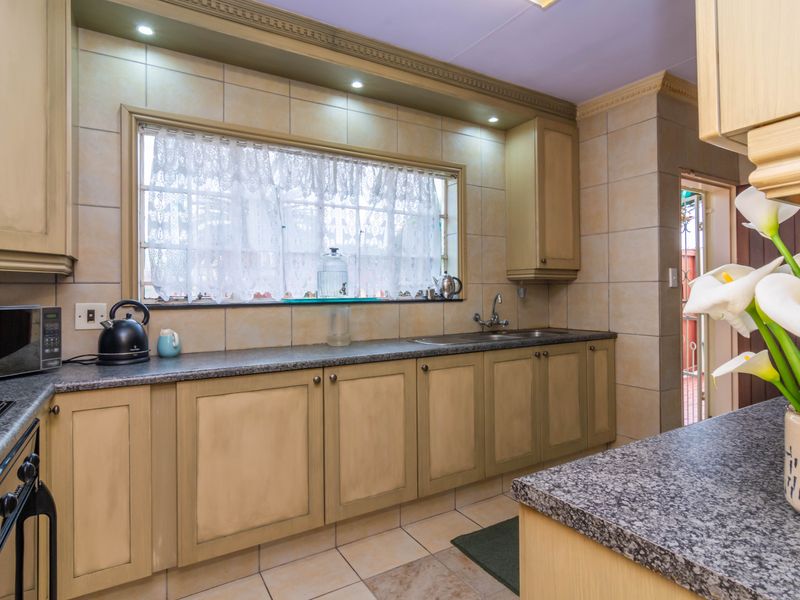 A functional kitchen featuring built-in cabinetry, granite countertops, a double sink, and tiled finishes, offering a classic layout with ample storage space.