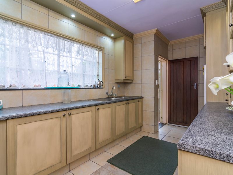 A functional kitchen featuring granite countertops, ample built-in cabinetry, tiled splashbacks, and a stainless steel sink with a view through the window.