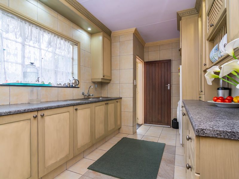 A functional kitchen featuring light-toned built-in cabinetry, granite countertops, tiled splashbacks, and tiled flooring with a classic timber door.