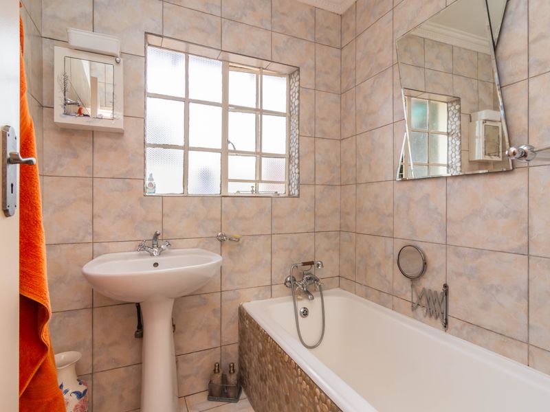 A functional bathroom featuring a pedestal basin, bathtub with mixer tap, and tiled wall finishes.