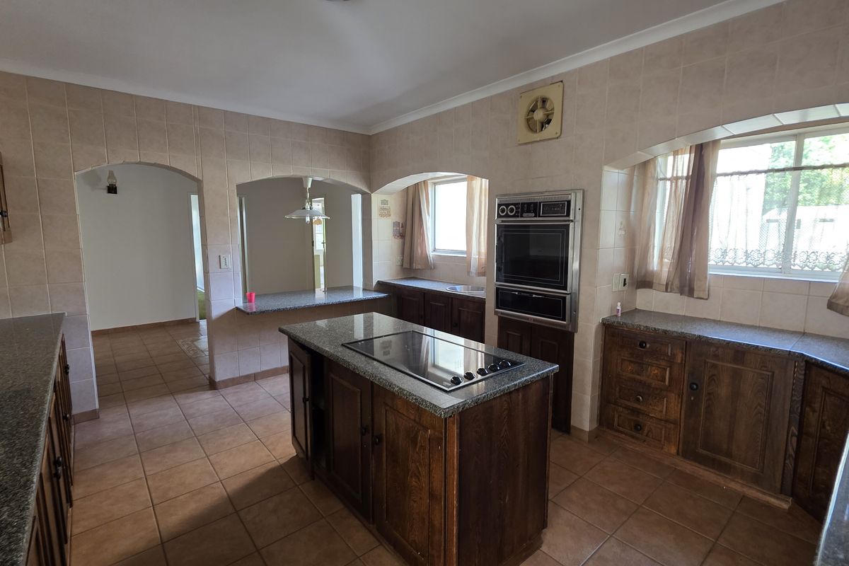 Spacious kitchen featuring dark wood cabinetry, granite countertops, a central island with a built-in hob, and integrated wall oven.