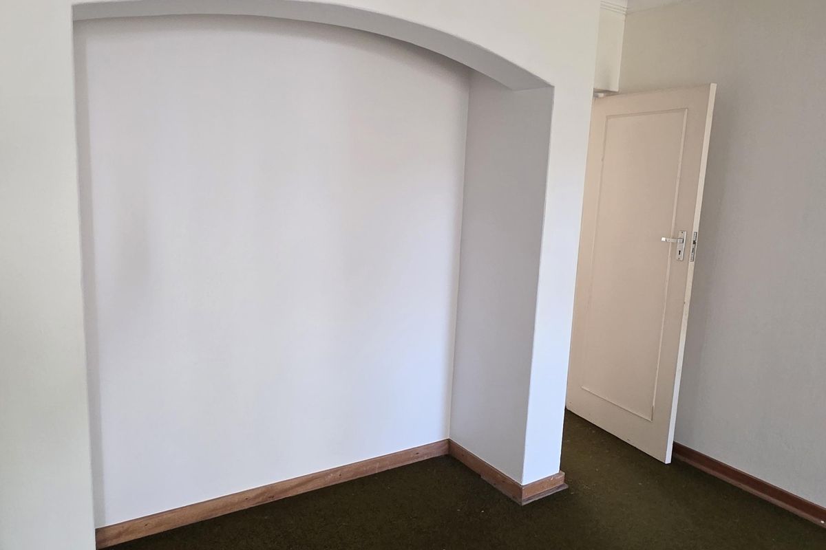An empty bedroom featuring a decorative arched alcove, crown molding, and dark carpeting, offering a blank canvas for renovation.