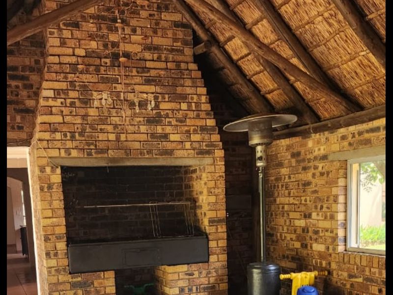 Covered outdoor patio area featuring a rustic brick fireplace and traditional thatched roof with exposed timber rafters.