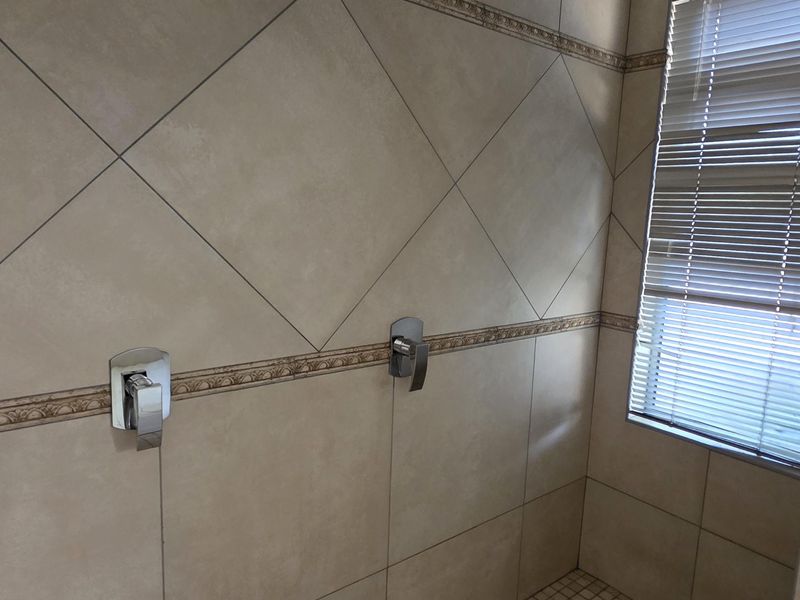 A spacious walk-in shower featuring dual rainfall shower heads, modern chrome mixers, and neutral-toned wall and floor tiling.