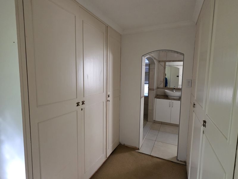 A hallway featuring extensive built-in cupboard storage and an arched entryway leading into a bathroom area.