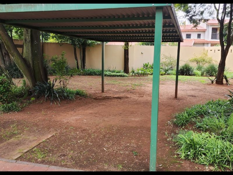 A spacious garden area featuring a metal carport structure, perimeter walling, and established trees with potential for landscaping improvements.