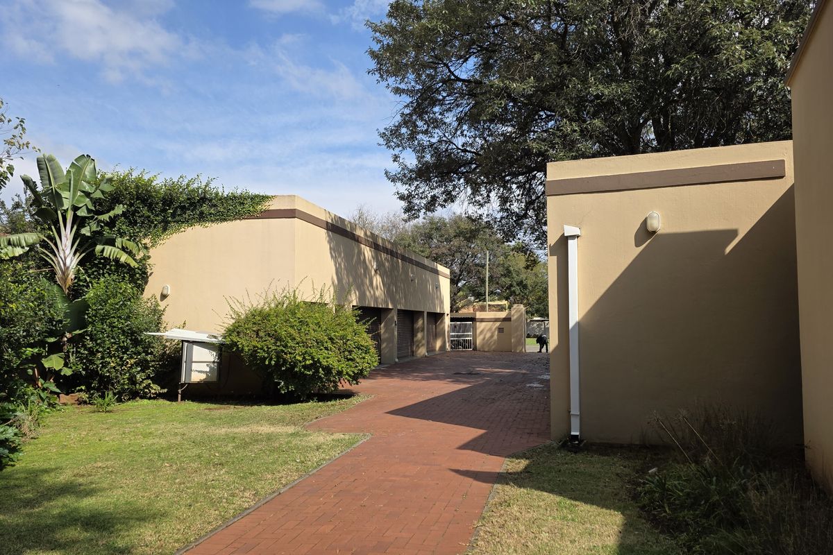 A view of the rear exterior area featuring a paved driveway, brick walkway, and established garden landscaping alongside the building structure.