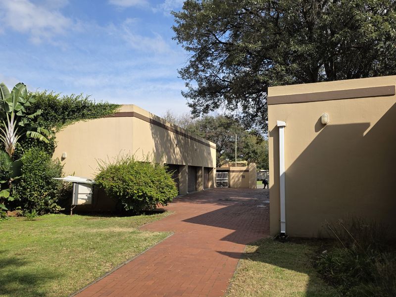 A view of the rear exterior area featuring a paved driveway, brick walkway, and established garden landscaping alongside the building structure.