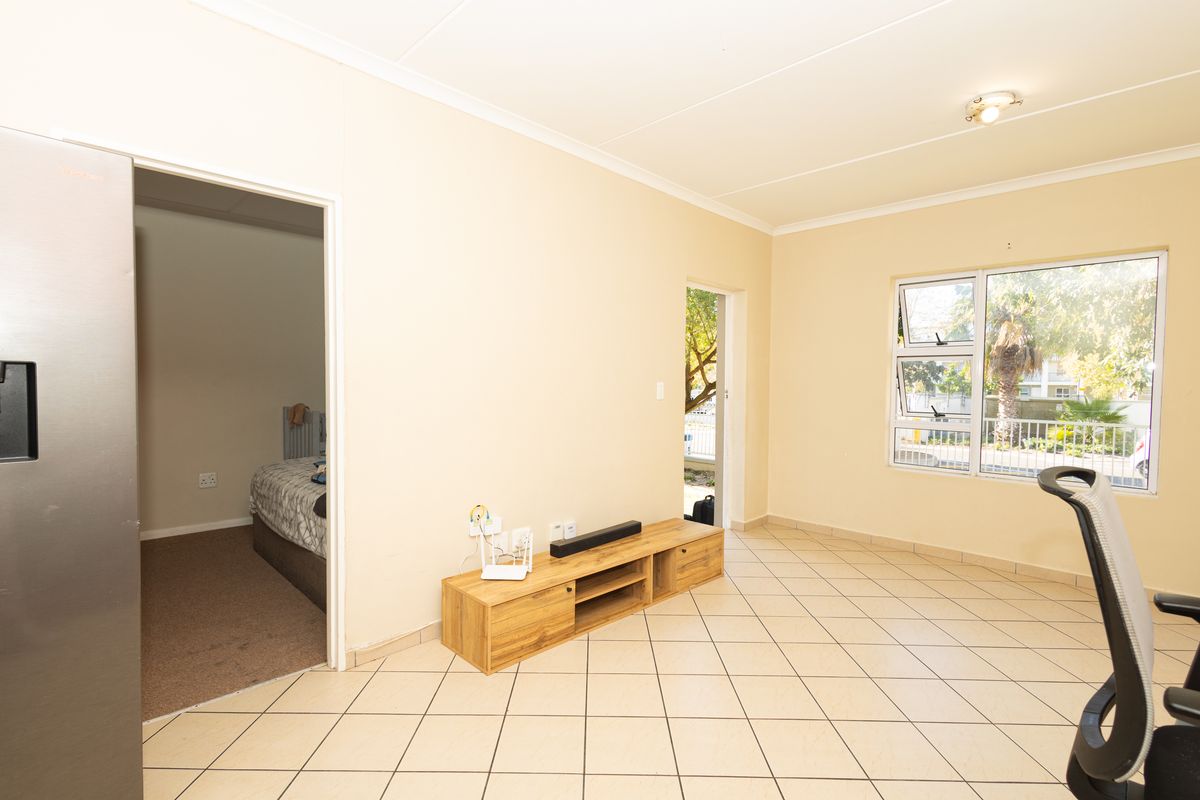 A bright living area featuring neutral tiled flooring, coved ceilings, and aluminium-framed windows, providing a clean and functional space with access to adjacent rooms.