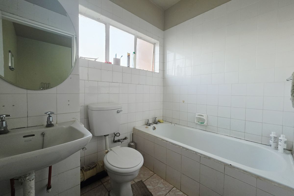 A dated bathroom featuring a standard bathtub, pedestal basin, and toilet with white wall tiling and original floor finishes.