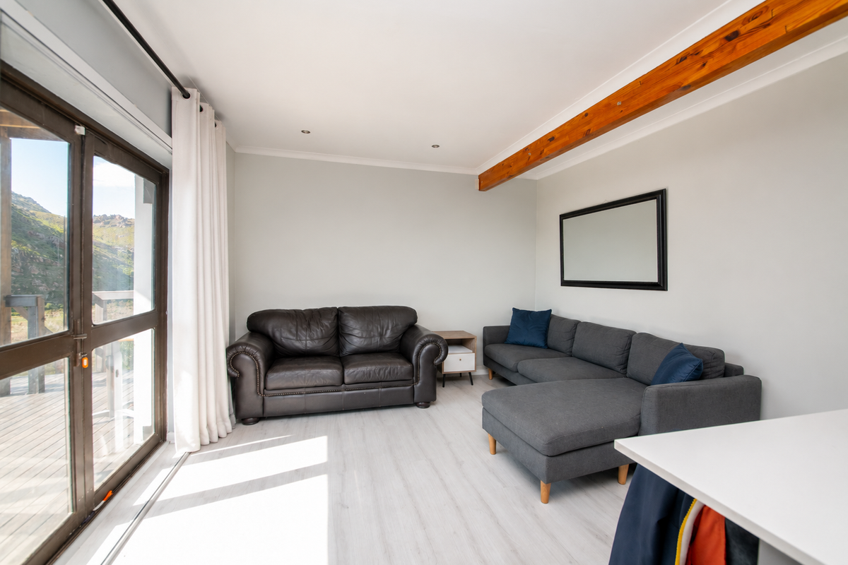 A bright living room featuring light laminate flooring, an exposed timber ceiling beam, and large sliding glass doors providing access to an outdoor deck.