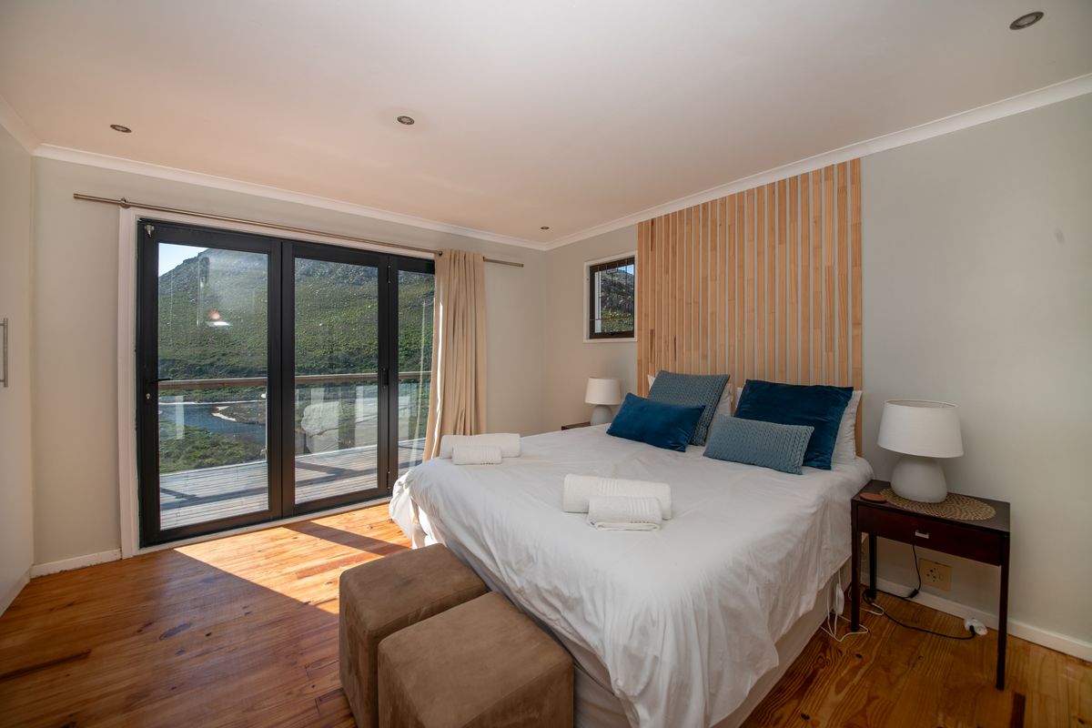 A bright bedroom featuring timber flooring, a decorative timber slat feature wall, and sliding glass doors opening to a scenic outdoor view.