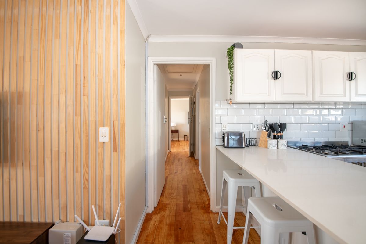 Modern kitchen featuring white cabinetry, subway tile backsplash, stone countertops, gas hob, and a decorative timber slat wall, leading into a hallway.