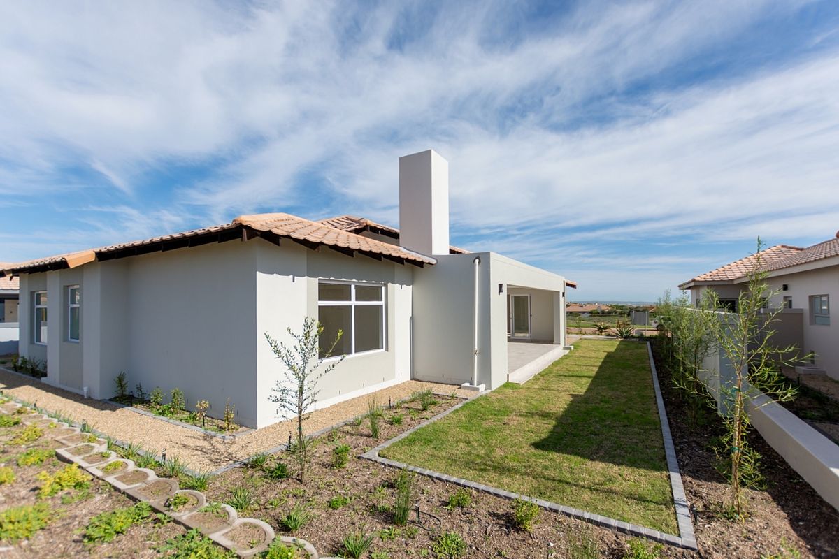 Rear view of a modern house featuring a tiled roof, chimney, covered patio, and a well-maintained landscaped garden with paved pathways.