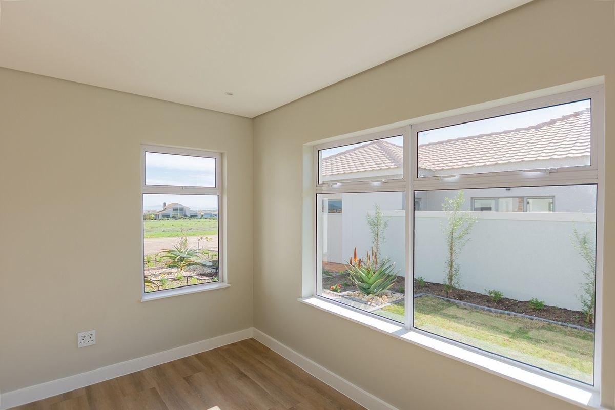 A bright, empty bedroom featuring modern laminate flooring and large aluminium-framed windows overlooking the garden.