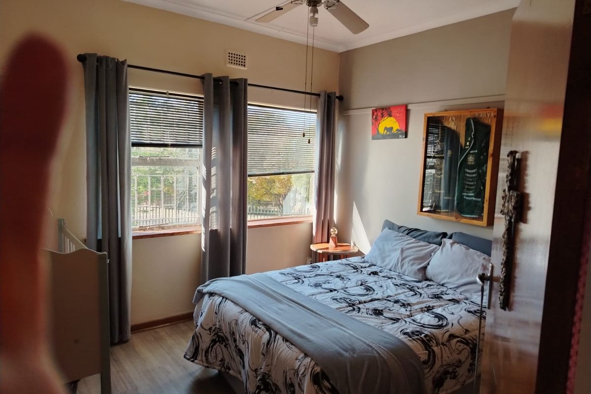 A cozy bedroom featuring laminate flooring, a ceiling fan, and large windows with blinds, providing natural light and a view of the exterior.