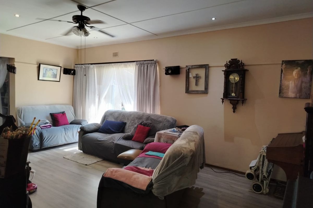 A spacious living room featuring light-toned laminate flooring, a ceiling fan, and large windows allowing natural light into the area.