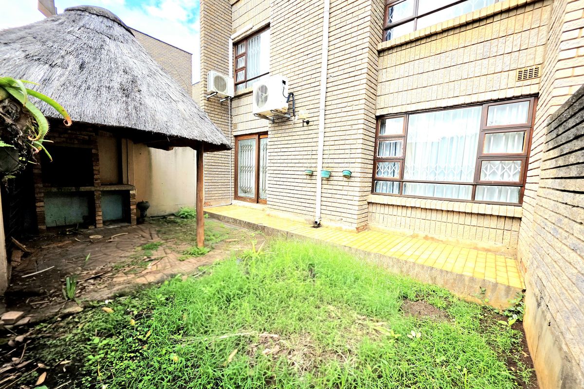 Rear exterior view of the apartment featuring a brick facade, a thatched lapa with a built-in braai, and a small garden area.