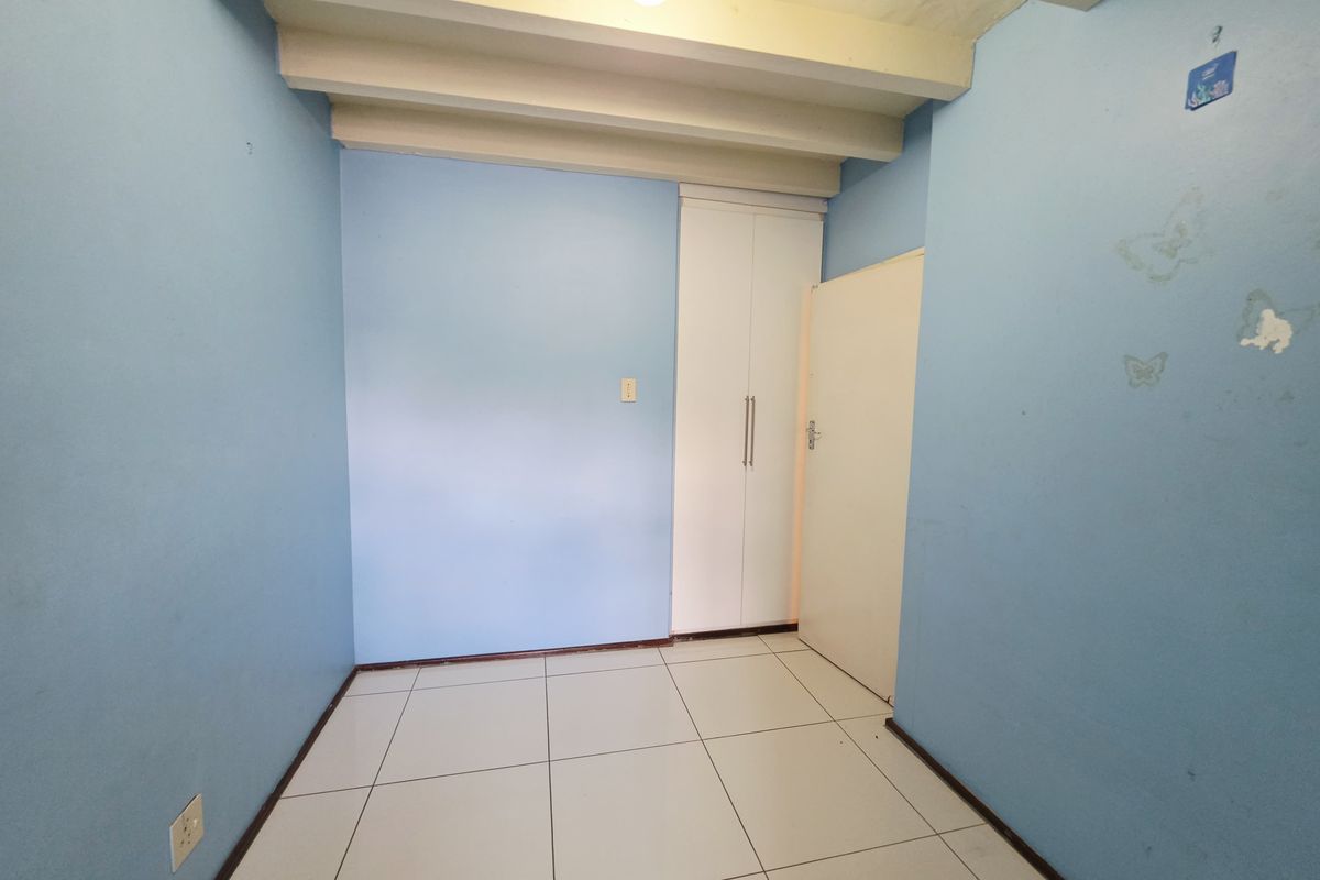 An empty bedroom featuring tiled flooring, exposed ceiling beams, and a built-in wardrobe, ready for a fresh coat of paint and new styling.