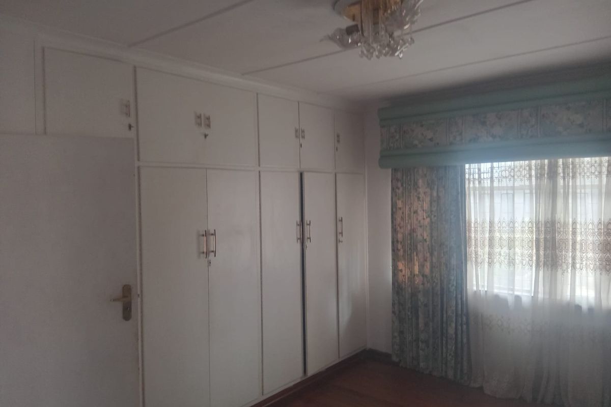 A bedroom featuring extensive built-in floor-to-ceiling cabinetry, wooden flooring, and a window with decorative pelmet and curtains.
