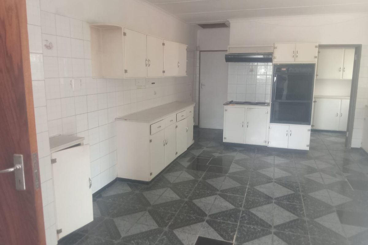 A spacious, dated kitchen featuring white cabinetry, built-in oven, extractor fan, and patterned floor tiles, offering significant potential for modernization.