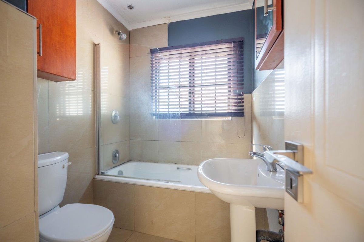 A functional bathroom featuring a pedestal basin, toilet, and a bathtub with a glass shower screen and tiled wall finishes.