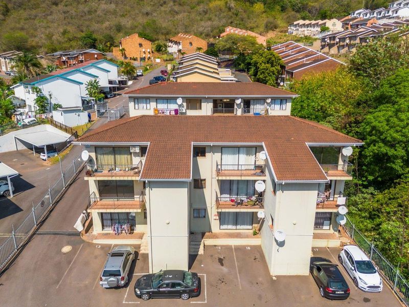 Aerial view of a multi-story townhouse complex featuring tiled roofing, private balconies, and an adjacent paved parking area within a fenced estate.