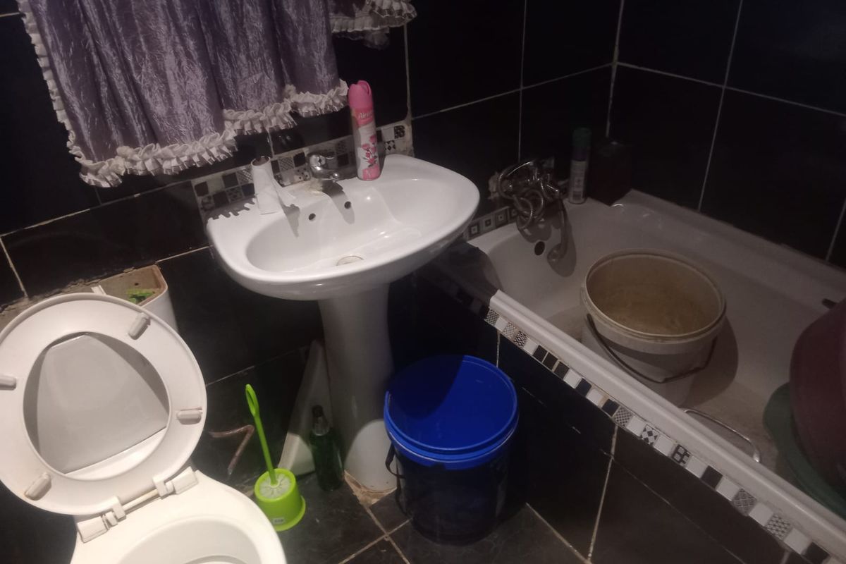 A compact bathroom featuring a pedestal basin, bathtub, and toilet with dark tiled walls and flooring, requiring cosmetic updates to improve its overall condition.