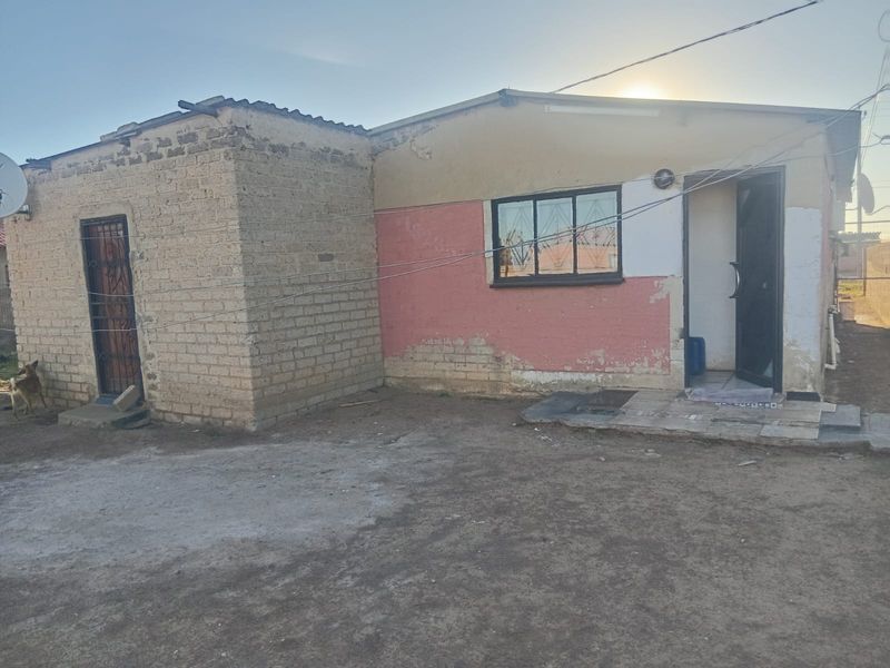 Rear exterior view of a single-story house featuring exposed brickwork, painted plaster walls, and security gates on the entrance and window.