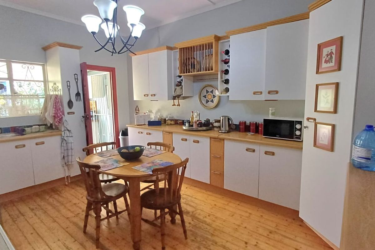 A functional kitchen featuring white cabinetry with timber accents, warm timber flooring, and direct access to the exterior via a security gate.